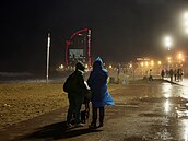 Pár se prochází po plá�i La Barceloneta, zatímco za nimi v Barcelon� nará�ejí...