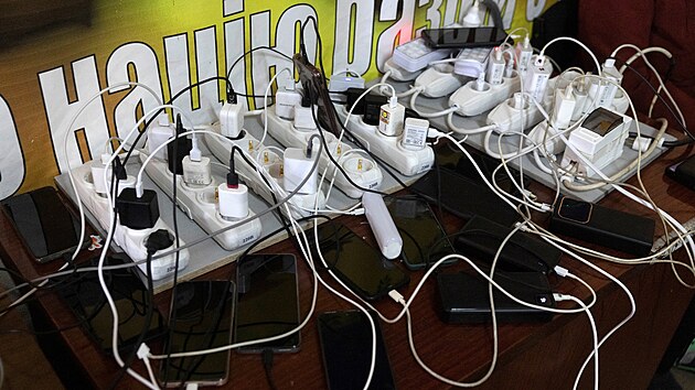 Lid� v Kyjev� se oh��vaj�, zat�mco �ekaj� na nabit� sv�ch mobil� ve vl�dn�m �tulku, kter� nab�z� z�kladn� slu�by a vyt�p�n� b�hem v�padk� proudu. (10. ledna 2026)