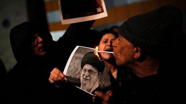 Demonstrant zapaluje cigaretu ho��c�m plak�tem s vyobrazen�m nejvy���ho v�dce ajatoll�ha Al�ho Chamene�ho b�hem shrom�d�n� na podporu protivl�dn�ch protest� v �r�nu, v Holonu v Izraeli.  (14. ledna 2026)