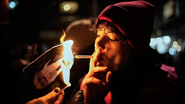 Demonstrant zapaluje cigaretu o ho��c� plak�t �r�nsk�ho nejvy���ho v�dce ajatoll�ha Al�ho Chamene�ho b�hem demonstrace v Berl�n�. (14. ledna 2026)