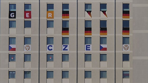 Okna budovy v olympijsk� vesnici zdob� vlajky v�prav v�etn� t� �esk�.