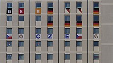 Okna budovy v olympijské vesnici zdobí vlajky výprav v�etn� té �eské.