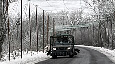 Vojenské auto oplocené elektrickou sítí na silnici s protidronovou sítí v...