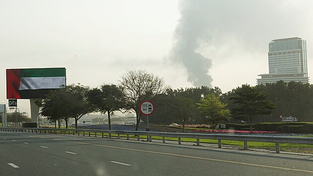 P�es �eln� sklo vozidla je vid�t kou� stoupaj�c� z Mezin�rodn�ho leti�t� v Dubaji pot�, co �tok dronem zas�hl palivovou n�dr�. (16. b�ezna 2026)