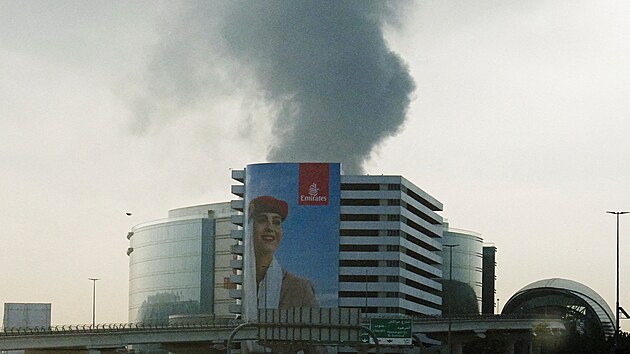 P�es �eln� sklo vozidla je vid�t kou� stoupaj�c� z Mezin�rodn�ho leti�t� v Dubaji pot�, co �tok dronem zas�hl palivovou n�dr�. (16. b�ezna 2026)