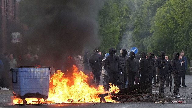 Maskovan� demonstranti stoj� u ho��c�ch kontejner� na ulici Ligoniel Road v severoirsk�m Belfastu. (9. �ervna 2026)