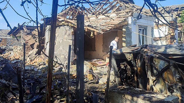 Civilista stoj� na m�st�, kde byl d�m t�ce po�kozen rusk�m dronov�m �tokem v r�mci rusk� invaze na Ukrajinu, v Mykolajivu na Ukrajin�. (12. �ervna 2026)