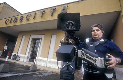 Kameraman stojí před vchodem do ateliérů Cinecittá.