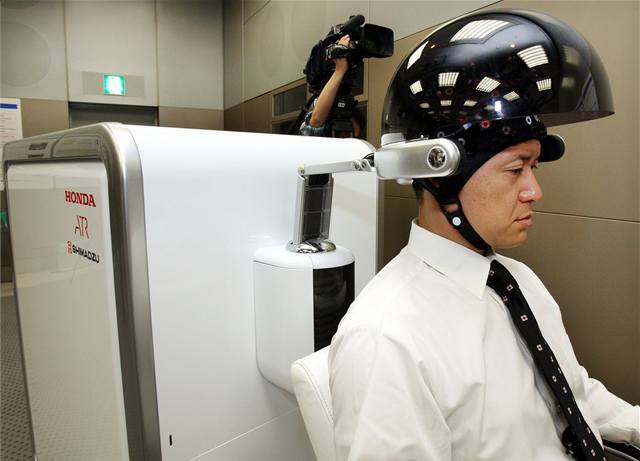 Zamstnanec firmy Honda zkouí zaízení. které propojuje mylenky v lidském mozku s robotem.