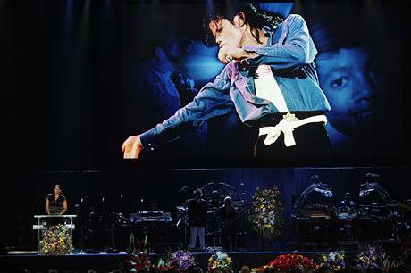 Poheb Michaela Jacksona. Na velkém pódiu mluví Queen Latifa, zatímco na obrazovce bely snímky Jacksona.
