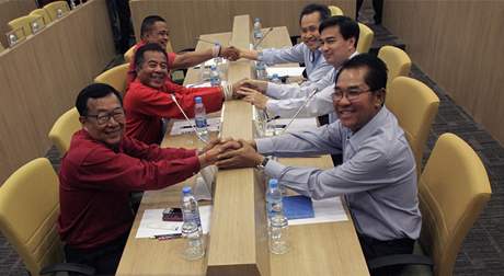 Thajský premiér (vpravo uprosted) Apchisit Vedadíva spolu se svými spolupracovníky potásá rukama Rudým koilím - opozici UDD.