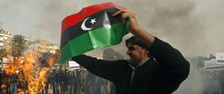 Demonstrant v Benghází s libyjskou vlajkou. V pozadí protestující pálí Kaddáfího Zelenou knihu.