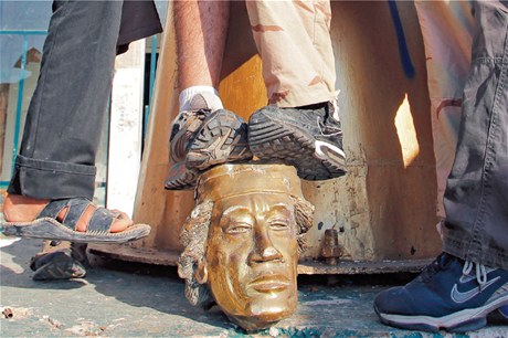 Rebelové stojící na hlav sochy Kaddáfího, zniené v jeho sídle. 