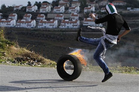 Palestinec 'posílá' hoící pneumatiku na izraelský check-point na Západním behu. 