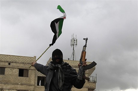 Bývalý syrský voják, který dezertoval k povstalcm, mává vlajkou a svou zbraní.