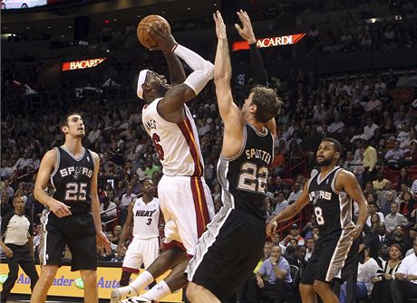 Miami Heat LeBron James (uprosted v bílém dresu) skóruje zatímco mu brání hrá San Antonia Spurs Tiago Splitter (22)