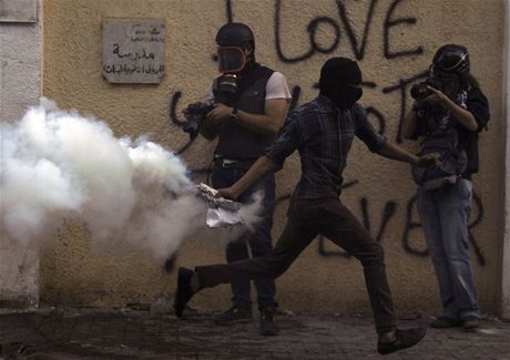 Fotografové vybaveni plynovými maskami fotí demonstranta, který bhem prostest v Káhie útoí na policii její vlastní  zbraní: slzným plynem   
