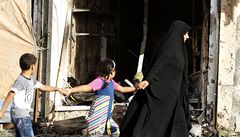 Žena s dětmi prochází kolem domu, který poničila bomba explodující v autě.