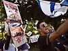 Izraelka drí transparent s fotkami následk teroristických útok, mu vedle ní mává izraelskou vlajkou