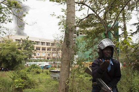 Keňský policista stojí před dobchodním domem, ze kterého stoupá dým