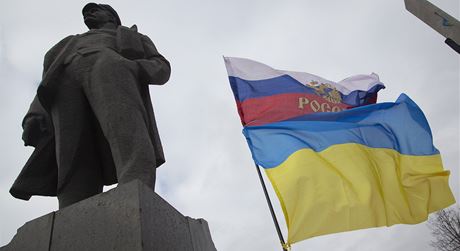 Vlajíí ukrajinská a ruská vlajka vedle sochy Vladimira Iljie Lenina.