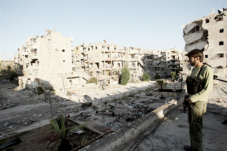 Bojovník opoziční Svobodné syrské armády pozoruje 12. srpna poškozené budovy a trosky na ulici předměstí severosyrského města Aleppo.