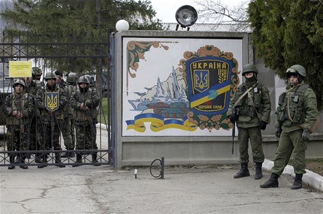 Ukrajintí vojáci (vlevo) a neoznaení vojáci (vpravo) steící bránu vojenské základny ve mst Privolnoye. 