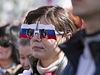 ena v brýlích ozdobených ruskou vlajkou sleduje projev ruského prezidenta Putina.