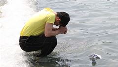 Píbuzný jednoho z poheovaných se modlí poté, co na hladinu moe vypustil papírovou lodiku se vzkazem.