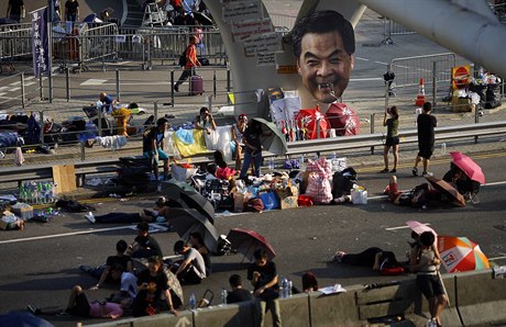 Demonstranti odpoívají v ulicích Hongkongu. Na sloupu visí vylepený portrét...