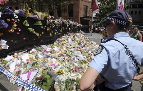 Policistka stojí ped záplavou kvtin, které pipomínají památku tragédie v...