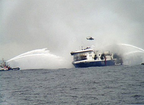 Záchranái v helikoptée krouí nad hoící lodí.