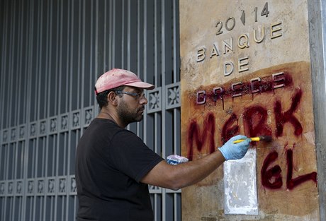 Zaměstnanec aténských technických služeb ničí dílo vandala, který název „Řecká...