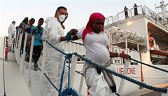 Pracovník italské pobřežní stráže pomáhá těhotné migrantce při vylodění...