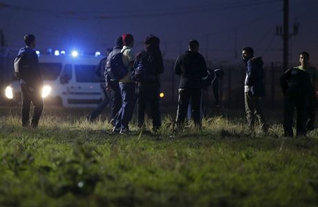 Migranti u plotu ohraniujcho pstup k Eurotunelu. V pozad policejn...