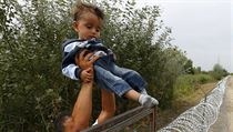 Překonávání překážek. Syrská uprchlice předává dítě přes plot, který začali...