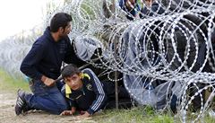 Uprchlíci ze Sýrie překonávají ostnatý plot na srbsko-maďarských hranicích.