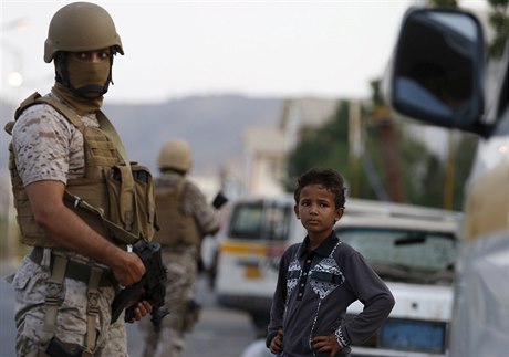 Jemenský chlapec vedle vojáka koalice vedené Saudskou Arábií, který drí hlídku...