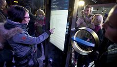 Lidé si prohlíjí dotykové monitory s jízdními ády v chytré zastávce MHD,...