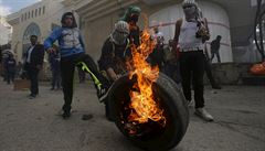 Palestintí protestující ped sebou tlaí hoící pneumatiku bhem stet s...
