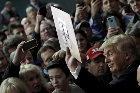 Donald Trump v obklopení svých pívrenc vystavuje ceduli s nalepenými...