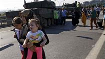 Žena se dvěma dětmi míjí tanky před nedaleko letiště v Istanbulu. Ozbrojený...