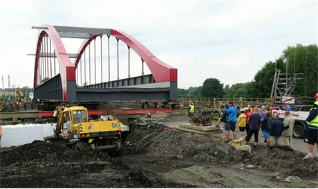 Stavbaři posouvají ocelovou konstrukci mostu.