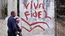 Lidé procházejí kolem grafiti. ‚Ať žije Fidel‘