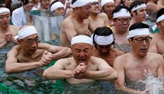 People wearing loin cloths pray as they bathe in ice-cold water outside the...