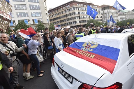 Auta na sob mla ruské vlajky a nápisy. Protestující se kolem nich...
