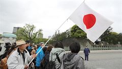 Mu drí japonskou vlajku, zatímco se lidé sházejí u císaského paláce v Tokiu.