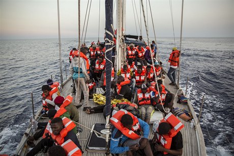 Televizní zábry ukázaly migranty sedící v adách na pídi lodi, na sob mají...