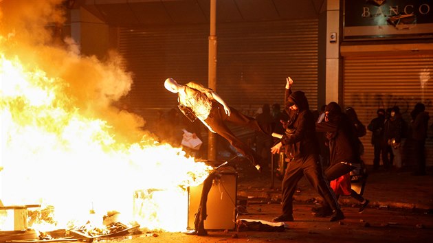 Protestující hází figurínu na obleení do pouliního ohn, který blokuje...