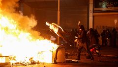 Protestující hází figurínu na obleení do pouliního ohn, který blokuje...